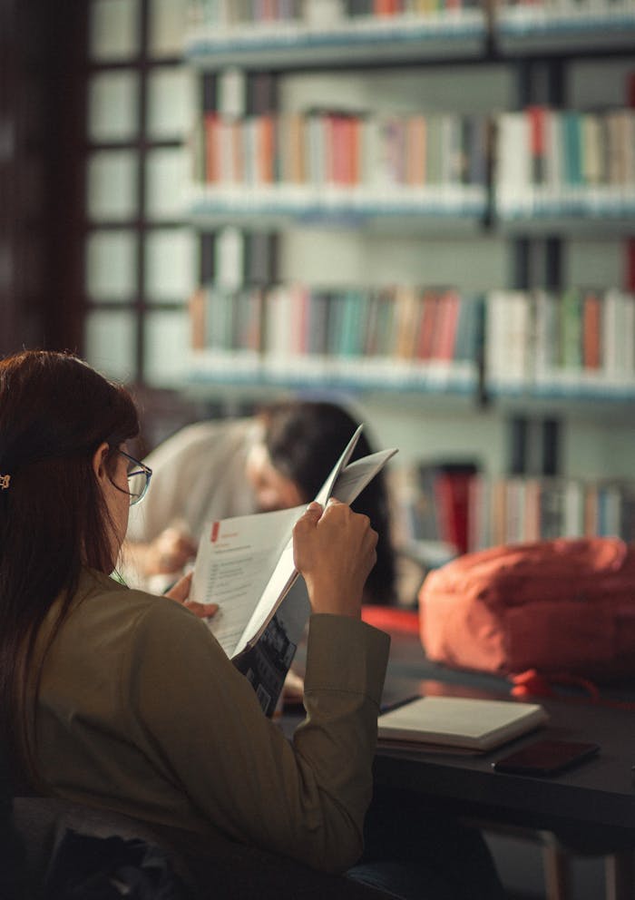 Adult woman reading in a cozy library setting, surrounded by bookshelves.